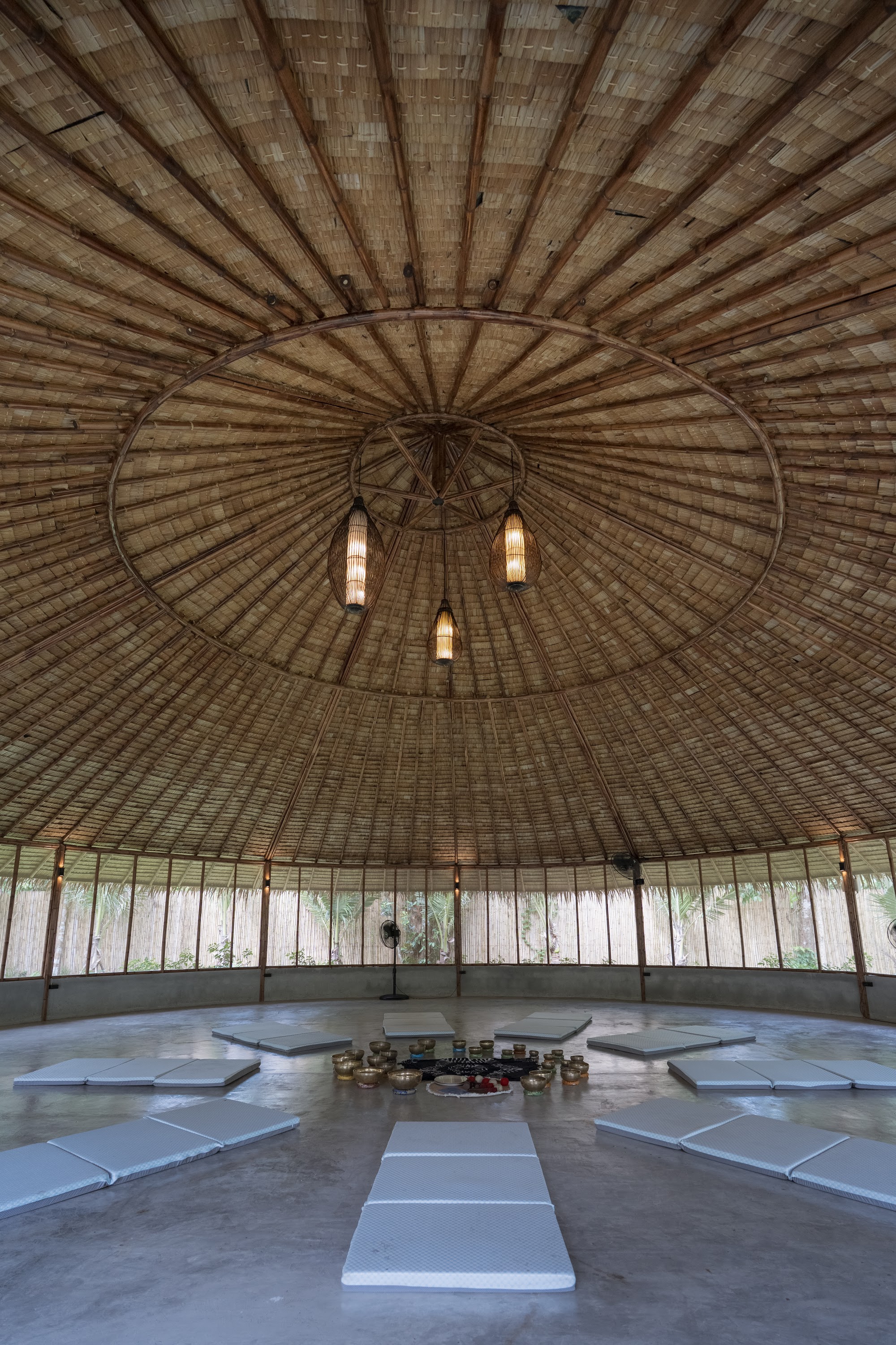 Inside the circular shala, mats and singing bowls arranged beneath the thatched roof